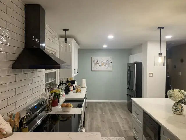 Remodeled galley kitchen with white subway tile, black wall-mounted range hood, white cabinets and wood-look floor